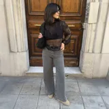 Pantalón de jean gris de corte ancho, con bolsillos delanteros con botón y cinturón negro.