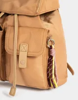 Mochila de tela color lila, con solapa con broche y tira de ajuste, doble bolsillo frontal con broche y pouch con charm lateral en forma de cartera.