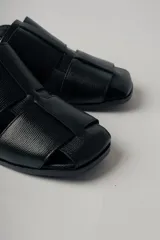 Sandalias negras de cuero con diseño de tiras entretejidas, puntera cuadrada, tira trasera con hebilla ajustable y tacón bajo cuadrado.
