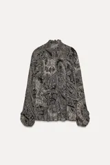 Camisa de viscosa con estampado paisley en blanco y negro. Cuello redondo con escote pico ajustable con cordones, mangas largas con elástico y volantes en los puños, bajo asimétrico y cierre frontal con botones forrados.