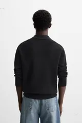 Polo negro de punto con cuello solapa y cierre frontal de cremallera.