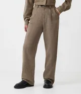 Pantalón de vestir de corte ancho, color marrón con textura tweed. Tiene cintura alta con trabillas, pliegues frontales, bolsillos laterales y un bolsillo trasero.