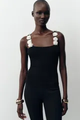 Top negro de punto con escote redondo y tirantes anchos decorados con flores blancas y abalorios.