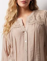 Blusa color beige de gasa, marca Figueroa & Flower. Cuello a la base, escote en V y abertura central con botones. Hombros y espalda en crochet. Manga 3/4 amplia con puño y botón.