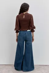 Blusa color marrón con cuerpo fruncido tipo nido de abeja, cuello alto con volados y mangas largas abullonadas con puños elásticos terminados en volados.