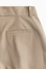 Pantalón color beige de corte holgado en sarga de algodón. Modelo de tiro alto con cierre, pretina prolongada con botón oculto y corchetes, bolsillos al bies y bolsillos insertados atrás. Piernas rectas con pinzas y pliegues adelante y atrás.