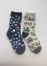 Pack de dos pares de medias de media caña con motivos de dinosaurios y huellas de dinosaurios. Un par es de color azul marino con huellas blancas y huesos. El otro par es de color gris con dinosaurios de colores y plantas.