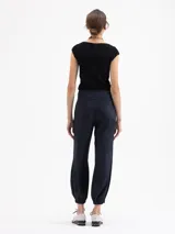 Pantalón negro de viscosa con ligero brillo, estilo babucha, con cintura alta y puños ajustados con elástico en los tobillos. Posee bolsillos diagonales delanteros y ojales traseros.