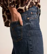 Pantalón de jean de corte recto con cintura alta, color azul oscuro, con bolsillos delanteros y traseros. Se ajusta a la cintura con cinturón de cuero marrón.