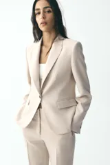 Blazer negra de corte clásico, con cuello solapa, manga larga, bolsillos frontales con solapa y cierre frontal con un botón.