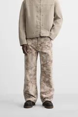 Pantalón de jean de corte recto con estampado abstracto en tonos beige, marrón y gris.