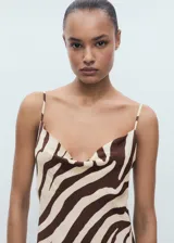 Vestido midi con estampado animal print de cebra en tonos marrón y beige. Presenta tirantes finos ajustables y escote drapeado. El corte es recto y tiene cierre lateral invisible.