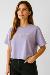 Remera lila de algodón con cuello redondo y mangas cortas. Presenta tres moños bordados en el frente.