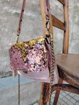 Cartera bandolera rectangular con solapa, cubierta de lentejuelas rosas y doradas. Incluye correa de cuero sintético rosa con tachas y correa de cadena dorada.