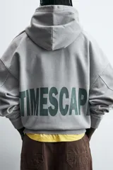 Sudadera gris con capucha ajustable, corte boxy fit, manga larga, bolsillo tipo canguro y estampado en la espalda.