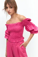 Crop top fucsia con escote off-shoulder, punto panal en el torso y volados en el escote. Mangas cortas elastizadas.