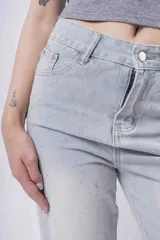 Jean de mezclilla celeste claro, corte wide leg y tiro alto, con pequeños apliques brillantes distribuidos por toda la prenda. El bajo está doblado.