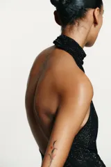 Top negro con cuello halter drapeado ajustable con botones y hombros descubiertos. Detalle de aplicación de strass combinado a tono. Forro interior y cierre en espalda con cremallera.