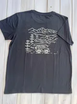 Remera negra de algodón y poliéster con cuello redondo y mangas cortas. Estampado en la espalda con dibujo lineal de montañas, cascada, árboles y camioneta con canoa en el techo.