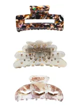 Set de tres pinzas para el pelo de plástico con diferentes diseños: una rectangular con estampado carey, una con forma de abanico con apliques de strass y una con forma de media luna con aberturas geométricas y estampado marmolado.
