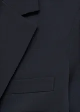 Blazer azul marino de corte entallado, con solapas de muesca, cierre frontal con un botón, hombros estructurados, dos bolsillos de ribete en la parte delantera y un bolsillo de ribete en el pecho.
