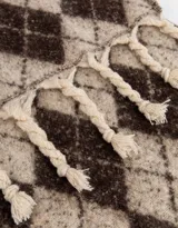 Bufanda tejida bicolor con terminación de borlas y tag de goma. Diseño de rombos en tonos marrón y beige.