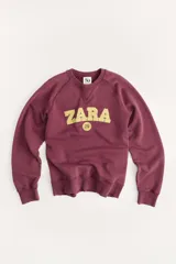 Sudadera de algodón color borgoña con cuello redondo y mangas largas. Estampado frontal con el texto "Zara" en color dorado y el número "75" en un círculo.