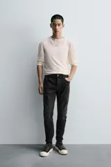 Pantalón de jean azul oscuro con efecto lavado y roturas en las rodillas, de corte ajustado al cuerpo desde la cintura hasta el tobillo.