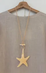 Collar largo con cordón de cuero color beige y dije de acrílico con forma de estrella de mar color crema.