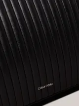 Bolso tote negro Calvin Klein, confeccionado en piel sintética acolchada con diseño de rayas verticales. Tiene doble asa de hombro, cierre superior con cremallera, herrajes plateados y logo metálico en el frente.