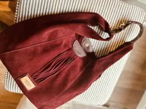 Cartera tipo hobo de gamuza color borgoña con flecos y asa corta de cuero marrón.