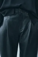 Pantalón de cuero negro de tiro medio, con pinzas delanteras, bolsillos laterales ocultos y corte holgado.