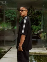 Chomba de tejido de punto cerrado color blanco, con cuello polo y mangas cortas. Presenta un bordado sutil en el frente y tres franjas negras en los hombros.