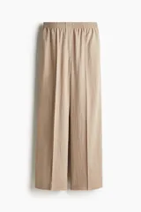 Pantalón de corte holgado color beige, confeccionado en sarga de mezcla de lyocell. Modelo de tiro alto con cintura fruncida, cierre decorativo y bolsillos laterales discretos. Piernas rectas con pliegues cosidos adelante y raya planchada atrás.