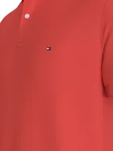 Chomba roja de Tommy Hilfiger, modelo 1985, de corte regular y mangas cortas. Tiene cuello tipo chomba, cartera de dos botones y logo bordado en el pecho. El cuello tiene un diseño de rayas. Confeccionada en mezcla de algodón y poliéster.