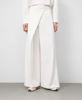 Pantalón blanco de pierna ancha y recta, estilo pareo, con cruce frontal envolvente y cintura elástica en la espalda. Presenta bolsillos laterales y falsos bolsillos traseros.