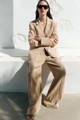 Pantalón color beige de lino, de tiro alto, con pinzas delanteras, bolsillos frontales y pernera ancha.