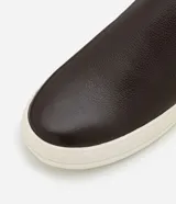 Championes slip on de cuero color marrón oscuro con detalle de cuero marrón claro en el talón y suela de goma color crema.
