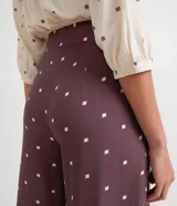 Pantalón pantacourt de viscosa color lila con estampado de pequeños cuadrados blancos. Tiene pinzas delanteras, bolsillos laterales y cierre con botones.