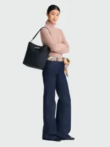 Bolso tipo hobo de cuero color negro, con asa de hombro ajustable y cierre superior con broche metálico.