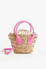 Cartera bandolera de paja color beige, con forro de tela color crema con cierre de cordón ajustable. Tiene dos asas cortas y correa larga ajustable de color rosa.