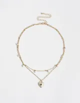 Collar corto dorado con doble cadena, una con eslabones y otra con perlas colgantes. Dije de corazón con strass incrustado.