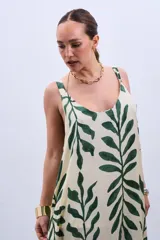 Vestido largo color crudo con estampado de hojas verdes, de corte amplio y breteles finos.