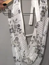 Top blanco de mesh con cuello halter y espalda descubierta, con apliques de lentejuelas y cuentas formando flores. Se ata al cuello y a la espalda con tiras finas.
