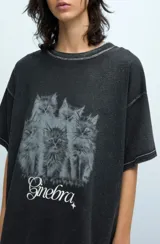 Remera negra de jersey de algodón peruano, con calce oversize, escote a la base y mangas cortas. Presenta un estampado de gatos y la palabra 'Ginebra' en el frente.