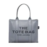 Bolso tote grande de cuero color gris con el texto "THE TOTE BAG MARC JACOBS" estampado en negro en el frente. Tiene doble asa de mano y cierre con broche a presión.