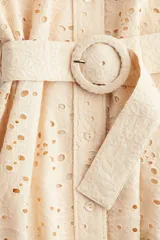 Vestido corto color beige con broderie, cuello camisero, botonadura frontal, cinturón extraíble con hebilla redonda, mangas globo largas con puños abotonados y ribetes festoneados.