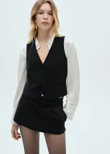 Chaleco negro de vestir con cuello en V, sin mangas y cierre frontal con botones. Presenta dos bolsillos delanteros de ribete y forro interior.