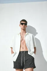 Traje de baño negro con estampado de palmeras blancas, con elástico y cordón en la cintura, bolsillos laterales y trasero con cierre autoadherente.