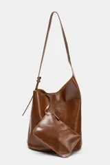 Bolso marrón de cuero, formato saca asimétrica. Tiene asa de hombro ajustable y cierre con imán. Incluye una cartera con bolsillo extraíble.
